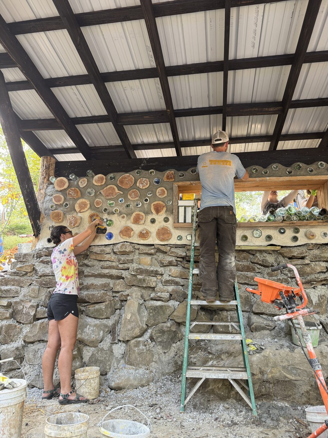 A student building a cordwood wall from a ladder