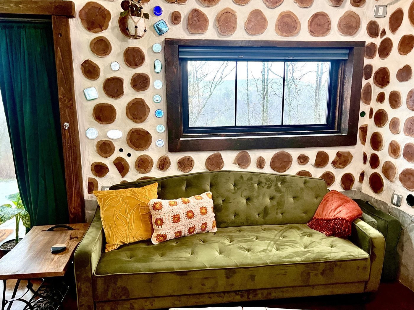 Goldfinch green velvet couch against a glass-bottle cordwood wall