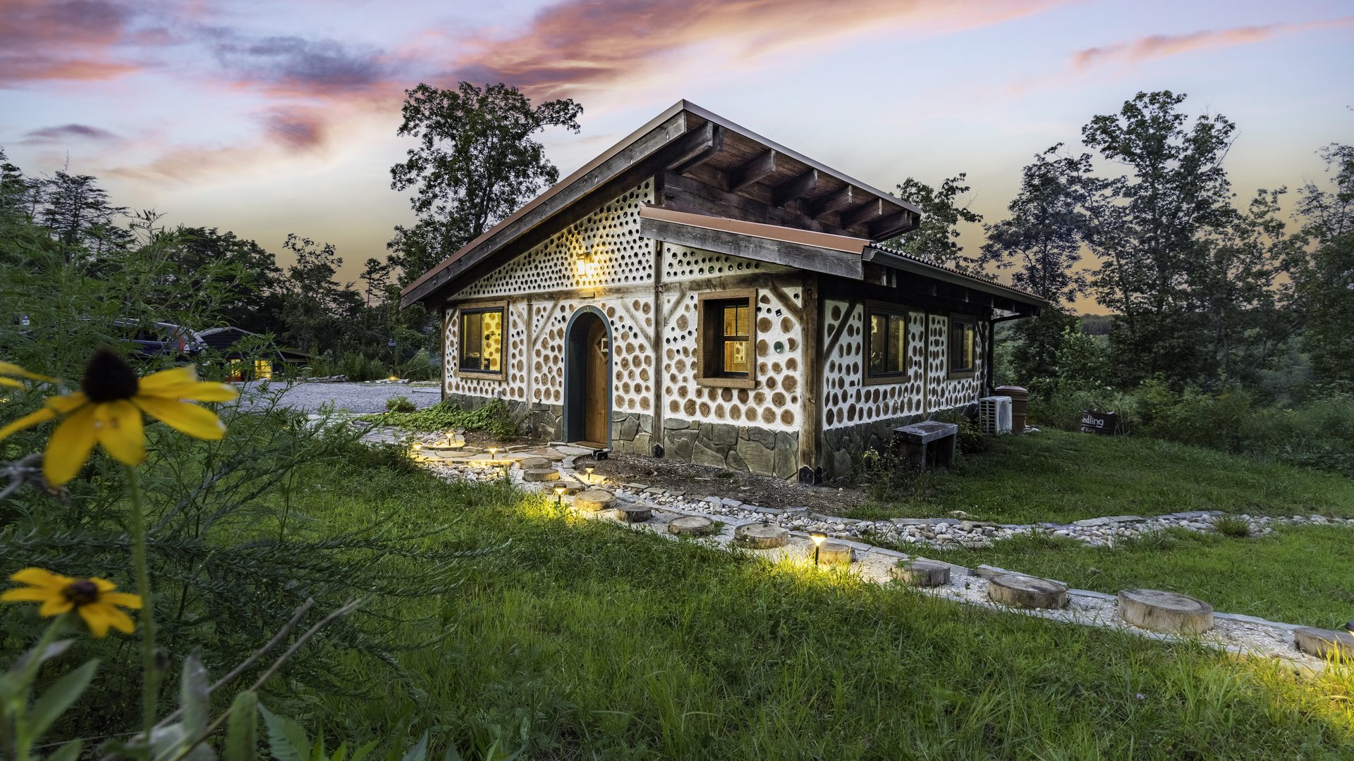 The Goldfinch cordwood cabin at dusk, its log-and-bottle walls glowing from within