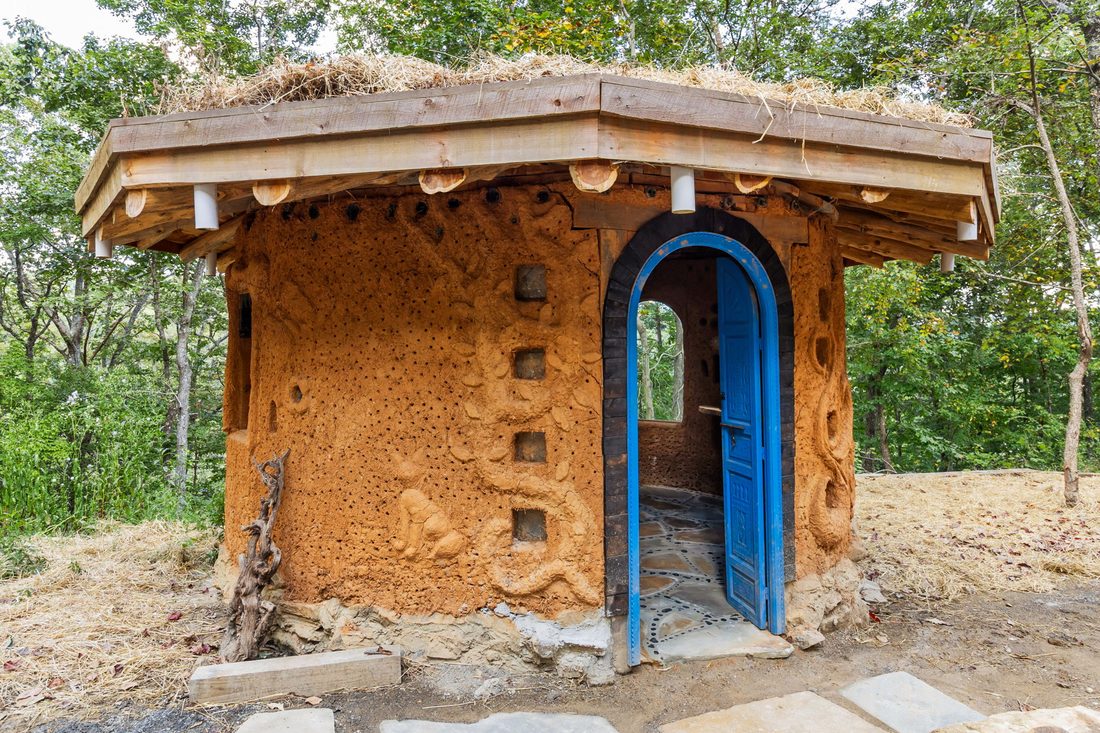 A hand-sculpted cob hut with a blue arched door