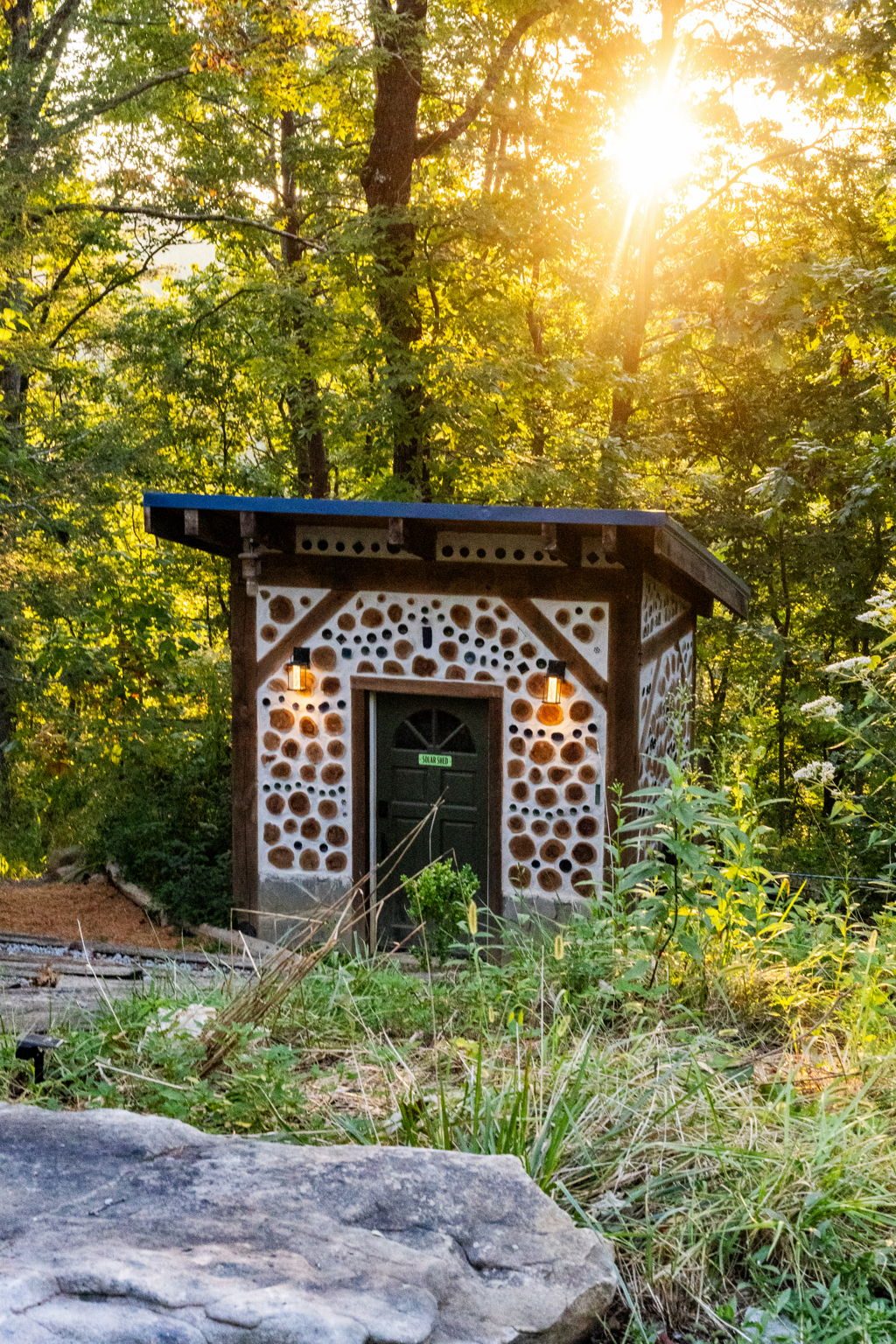 A cordwood hut with the sun breaking through the trees